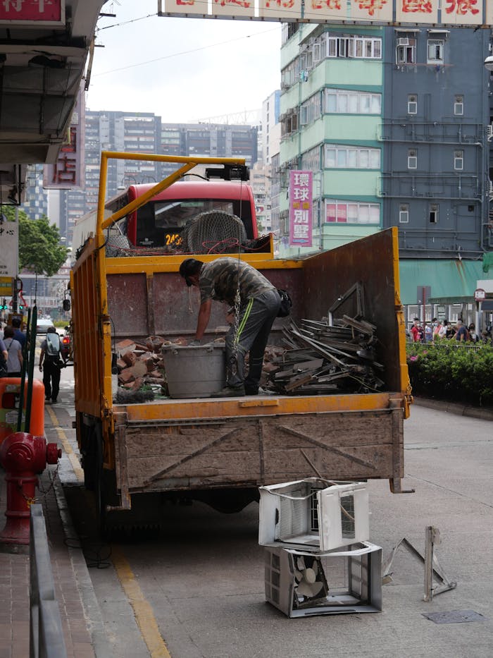 Man sorting and loading scrap metal onto a truck in a busy urban street scene.