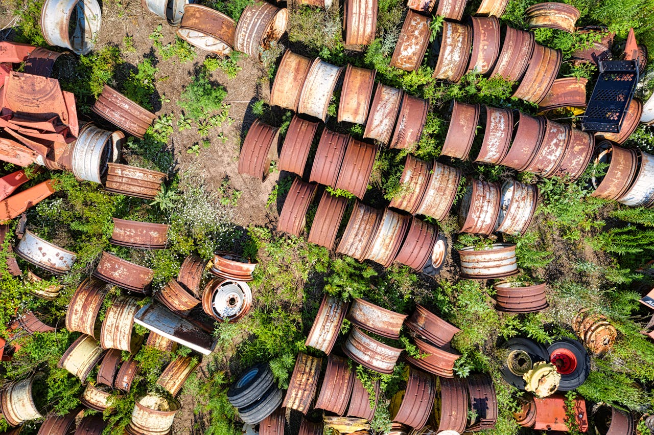 An aerial view showcasing rusty scrap rims scattered in a lush overgrown Wisconsin junkyard.